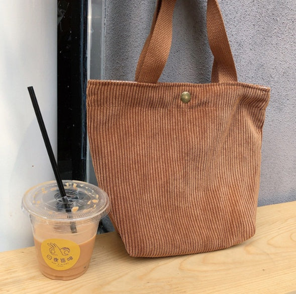 Brown corduroy tote bag on a wooden surface with a drink container next to it.