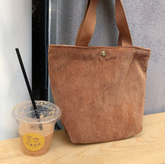 Brown corduroy tote bag on a wooden surface with a drink container next to it.