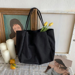 Black tote bag with yellow tulips on a textured surface with framed pictures and candles.