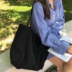 Person holding a black tote bag outdoors