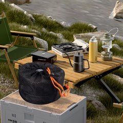 Camping setup with a table, chair, stove, and other gear by a body of water.
