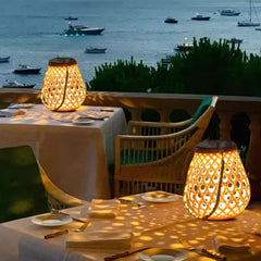 Outdoor dining setup with table, chairs, and illuminated lanterns overlooking a body of water with boats.