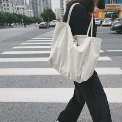 Person crossing a street with a white tote bag