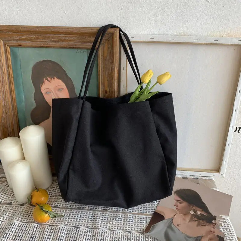 Black tote bag with yellow tulips on a textured surface with framed pictures and candles.