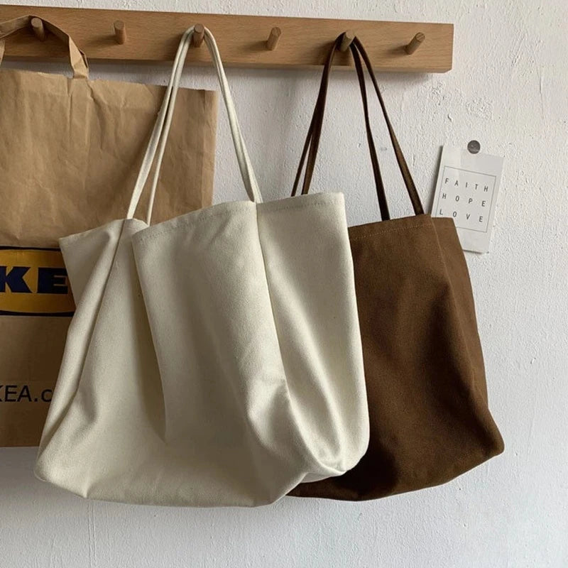 Two tote bags, one beige and one brown, hanging on a wooden rack against a white wall.