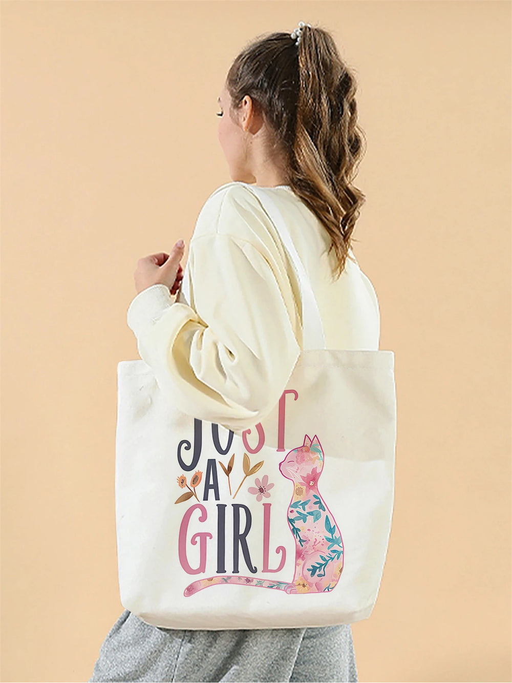 Person holding a tote bag with 'Just a Girl' design on a beige background