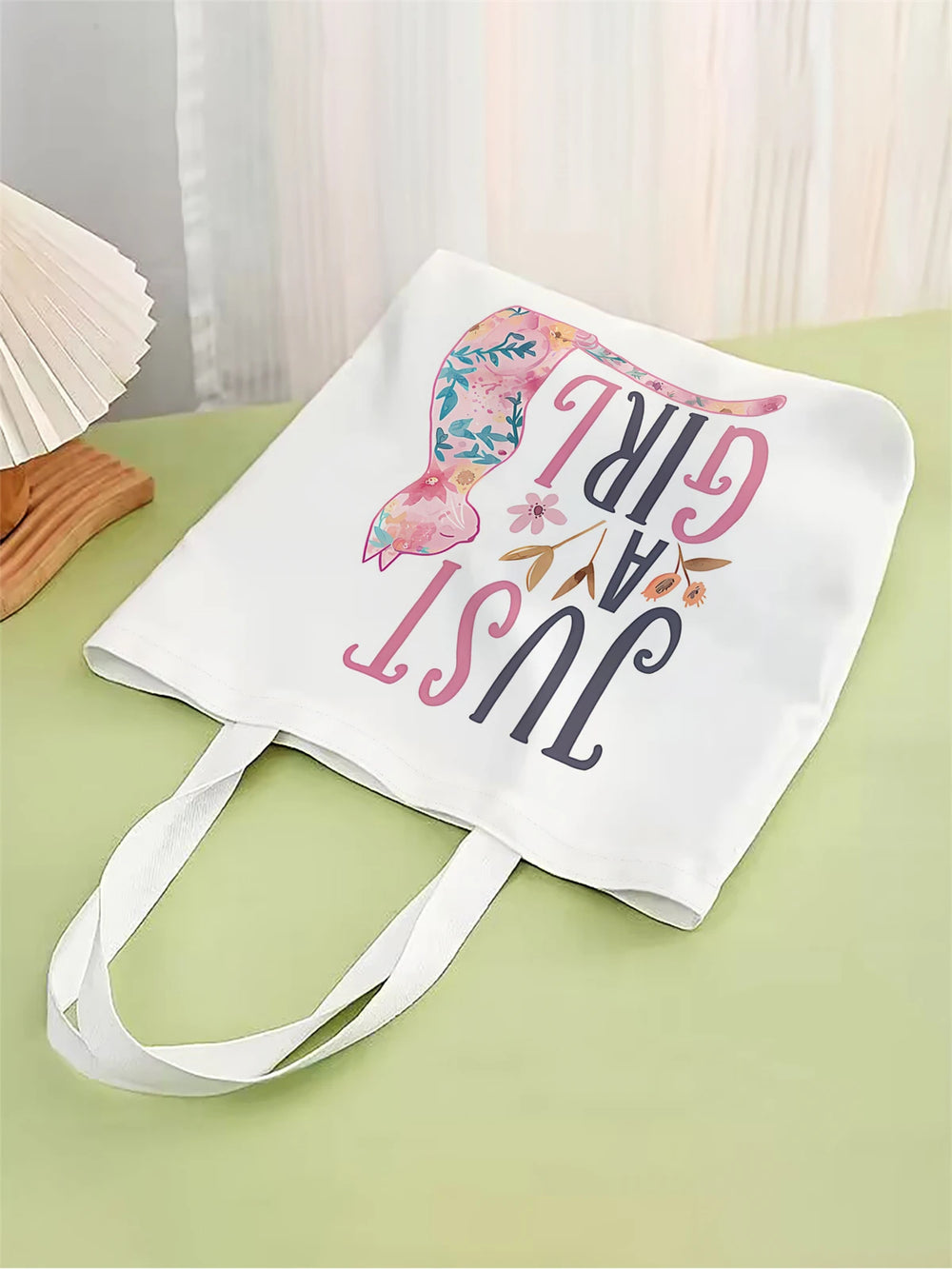 White tote bag with floral design and text on a green surface