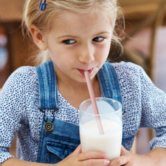 Young girl drinking from a glass with a straw in an outdoor setting